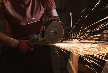 Sparks fly and cut metal. Angle grinder machine cuts metal in the dark, the lantern shines. The builder cuts a metal bar with a cutting wheel.