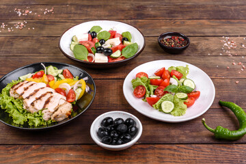 Three fresh delicious salads with chicken, tomato, cucumber, onions and greens with olive oil