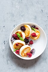 Fresh cottage cheese or ricotta  pancakes (syrniki,fritters) on a white plate with fresh berries on a blue background. Delicious healthy breakfast.  Ukrainian, Russian cuisine sweet food.