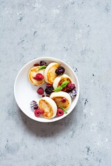 Fresh cottage cheese or ricotta  pancakes (syrniki,fritters) on a white plate with fresh berries on a blue background. Delicious healthy breakfast.  Ukrainian, Russian cuisine sweet food.