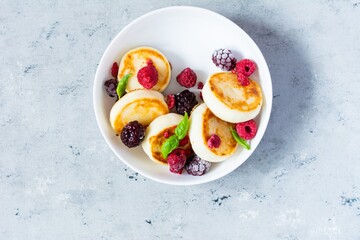 Fresh cottage cheese or ricotta  pancakes (syrniki,fritters) on a white plate with fresh berries on a blue background. Delicious healthy breakfast.  Ukrainian, Russian cuisine sweet food.