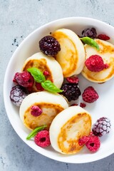 Fresh cottage cheese or ricotta  pancakes (syrniki,fritters) on a white plate with fresh berries on a blue background. Delicious healthy breakfast.  Ukrainian, Russian cuisine sweet food.