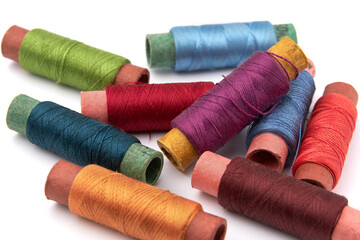 Many spools of thread of different colors scattered on a white background