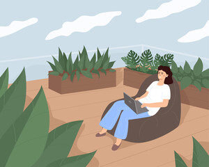 A young pretty woman is working or relaxing sitting in a cozy bag on the terrace, surrounded by greenery and plants in the rooftop garden.