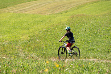 Girl child riding mountain bike on a green meadow in summer.