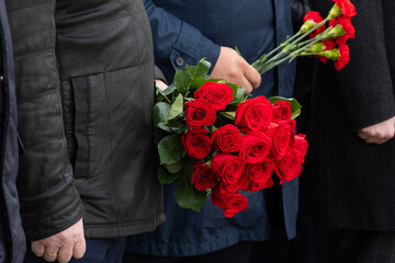 A man holds red rose flowers in his hands. A sad occasion. Laying flowers at monuments and graves.