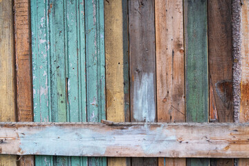 A fragment of a primitive wooden fence made of various old colored boards. There is a horizontal beam. Background. Texture.