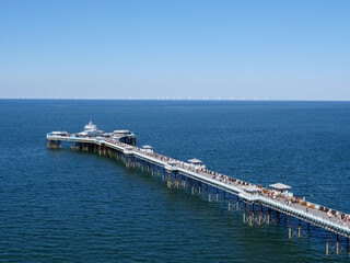 High angle view of Llandudno seaside resort pier in the blue sea and wind turbines by horizon