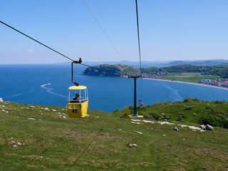 Yellow color overhead cable car with two unrecognizable people in it moving up from tourist resort town Llandudno to Great Orme hill top.
