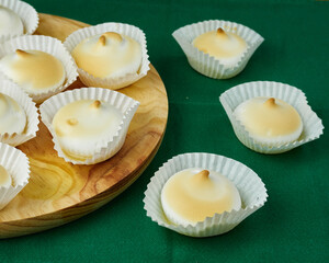 Several and Delicious French dessert Meringues into a silicone form moulds on a round wooden plate and the others on a green tablecloth