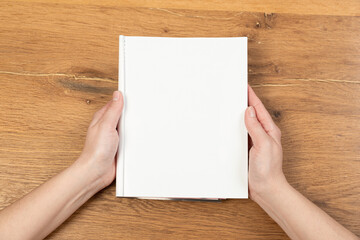 Obraz premium Woman holding brochure with blank cover on wooden background, top view. Mock up for design