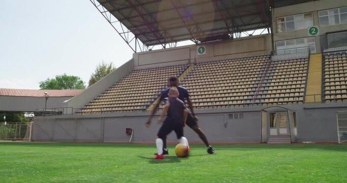 Diverse father and son playing football on stadium