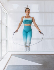 woman jumping rope with her hands open and knees bent. she is wearing blue tights and white...