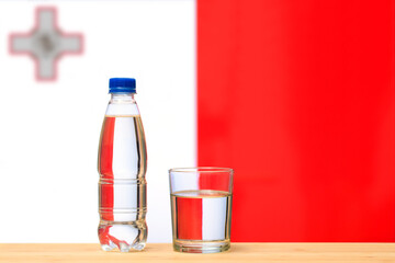 A bottle of clean drinking water and a glass stand on the table against the background of the flag...