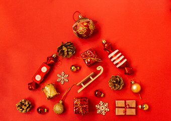 Flat composition with a Christmas tree made of different festive items, snowflakes, gifts, sweets, Christmas tree decorations on a red background. Copy space.