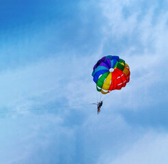 Two men are sailing on a colorful and bright parachute against the blue sky. Copy space.