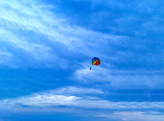 Two men are sailing on a colorful and bright parachute against the blue sky. Copy space.