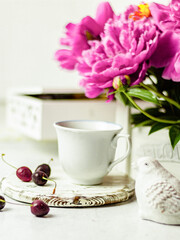 Shabby chic tea. A cup of tea on a white wooden tray with a cherry nearby. Peonies are in a white box. Blurred background