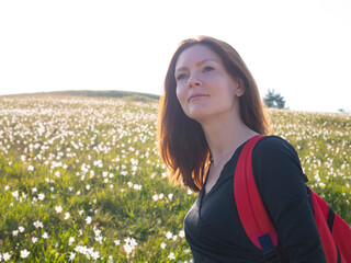 Woman with backpack travels in nature. A flower bed, meadow of white narcissus. Face of happy woman doing hiking.