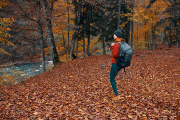 Naklejka na ściany i meble woman in autumn in the park with fallen leaves and a backpack on her back river in the background