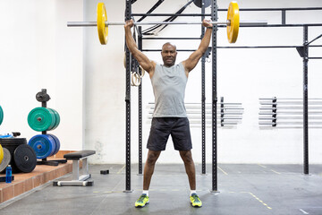 Black strong man lifting weights in fitness center. Physical training. Space for text.