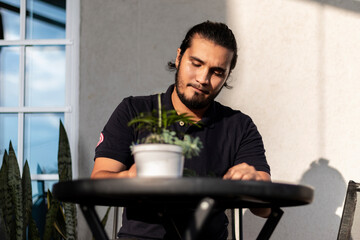 Young bearded latino man sitting in a black table with plants.