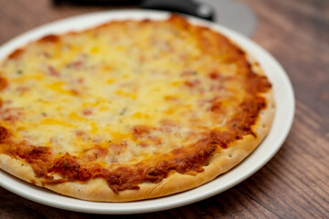 Close up and selective focus of a home cooked thin crust four cheese pizza on a white plate on a wooden table