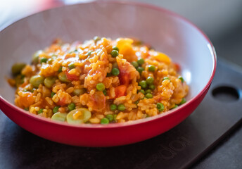 Close up of a healthy, nutritious and homemade vegetable paella in a red dinner bowl with selective focus, shallow depth of field and bokeh