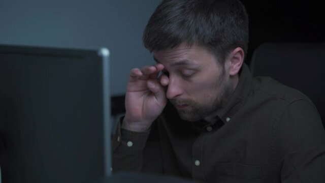 Home office. Handsome man working late at home. Tired young male feels pain, eye strain, dry irritated eyes, fatigue from working at monitor. Stressful frustrated person overworking at computer