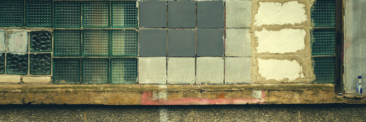 Old wall with a window made of square gray and glass tiles. Rough ribbed surface of dirty green glass. Vintage texture for background and design.
