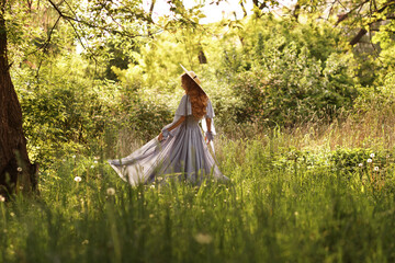 girl in a hat and dress in the garden in the summer sun on a walk