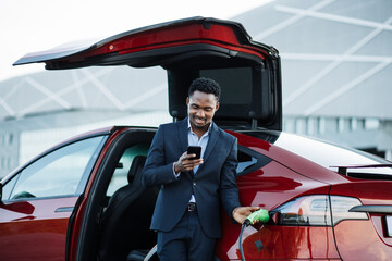 Handsome man in business suit surfing internet on modern smartphone while waiting electric car to...