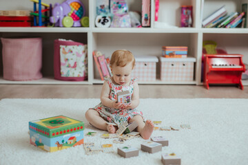 Little curious baby girl playing on a playground in a bright sunny room. Learning and playing colorful educational blocks game and puzzle