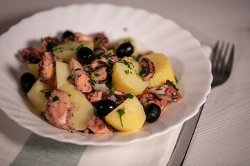 octopus salad with potatoes and olives in a white plate on a light gray table