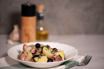octopus salad with potatoes and olives in a white plate on a light gray table