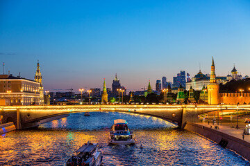 View of the Moscow Kremlin and Moscow City Skyscrapers along the quay of the Moscow river with sightseeing ships during evening sunset blue hour