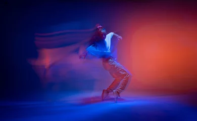 Poster Dancing female standing on tiptoe in colourful neon studio light. Long exposure. Contemporary hip hop dance © Georgii