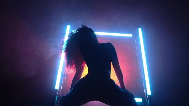Silhouette of hot woman dancer on smoky multi-colored glowing frame background. Neon spotlight shines behind lady. She moving seductively her body, buttocks and long hair.