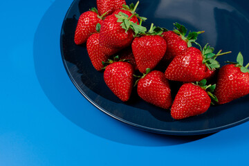 Bunch of strawberry on plate on blue background. Summer seasonal red berry.