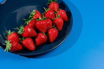Bunch of strawberry on plate on blue background. Summer seasonal red berry.