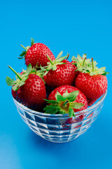 Bunch of strawberry in bowl on blue background. Yummy summer fruit.