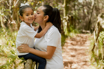 Hispanic mom kissing her little daughter in the park-loving mother hugging her daughter-happy latin family