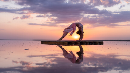graceful gymnast performs a flexible pose at sunset in the reflection of the water beautiful silhouette