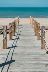 Fototapeta premium Wooden path on the beach over the sand with ocean view, during summertime. Wood walkway with ropes leading to beach scene.