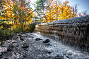 Autumn landscape with a small river and a waterfall at open locks in Vermont