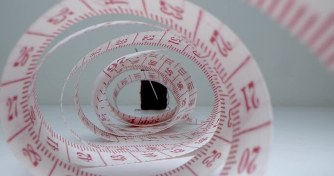 Super macro shot of a measuring tape into a roll of sewing and colored thread on the background stand.Garment factory. Needle, threads,measuring tape,spools of colored threads are visible in frame.