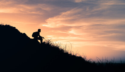 Silhouette of a person sitting on a mountain edge looking at the view. 