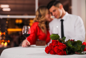 Lovely couple celebrating Valentine's day in restaurant, focus on table with red roses