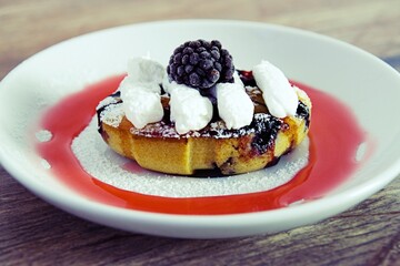 Sweet, juicy muffin with berries, sprinkled with vanilla sugar and whipped cream on top, with blackberries on a white and black plate