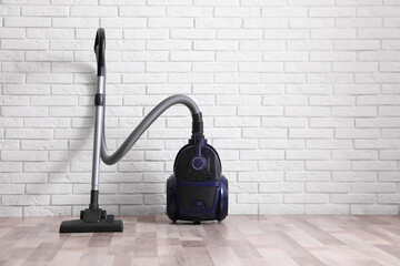 Modern vacuum cleaner near white brick wall indoors
